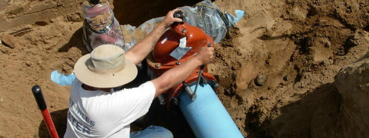 A worker adjusts and installs a valve on a blue pipe, part of an underground system.