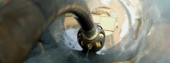 Close-up view inside a pipe with a dark rubber hose showing through, possibly part of a drainage system.