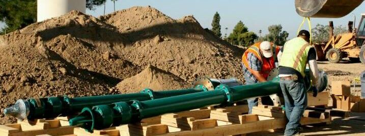 Workers prepare and inspect long green pump pipes in a construction area, ready for installation.